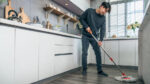 Young adult man mopping a kitchen floor.