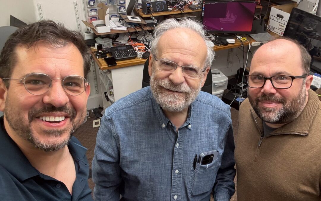 Selfie of Aaron Sylvan, Bob Frankston, and Brandon Vogel, left to right, in Bob's office in Newton, Massachusetts, with a workbench crowded with electronics behind them.