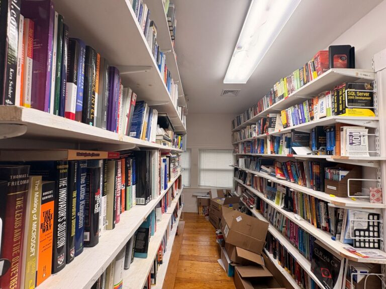 A narrow aisle between floor-to-ceiling shelves packed with technology and business books in Bob Frankston's lab.